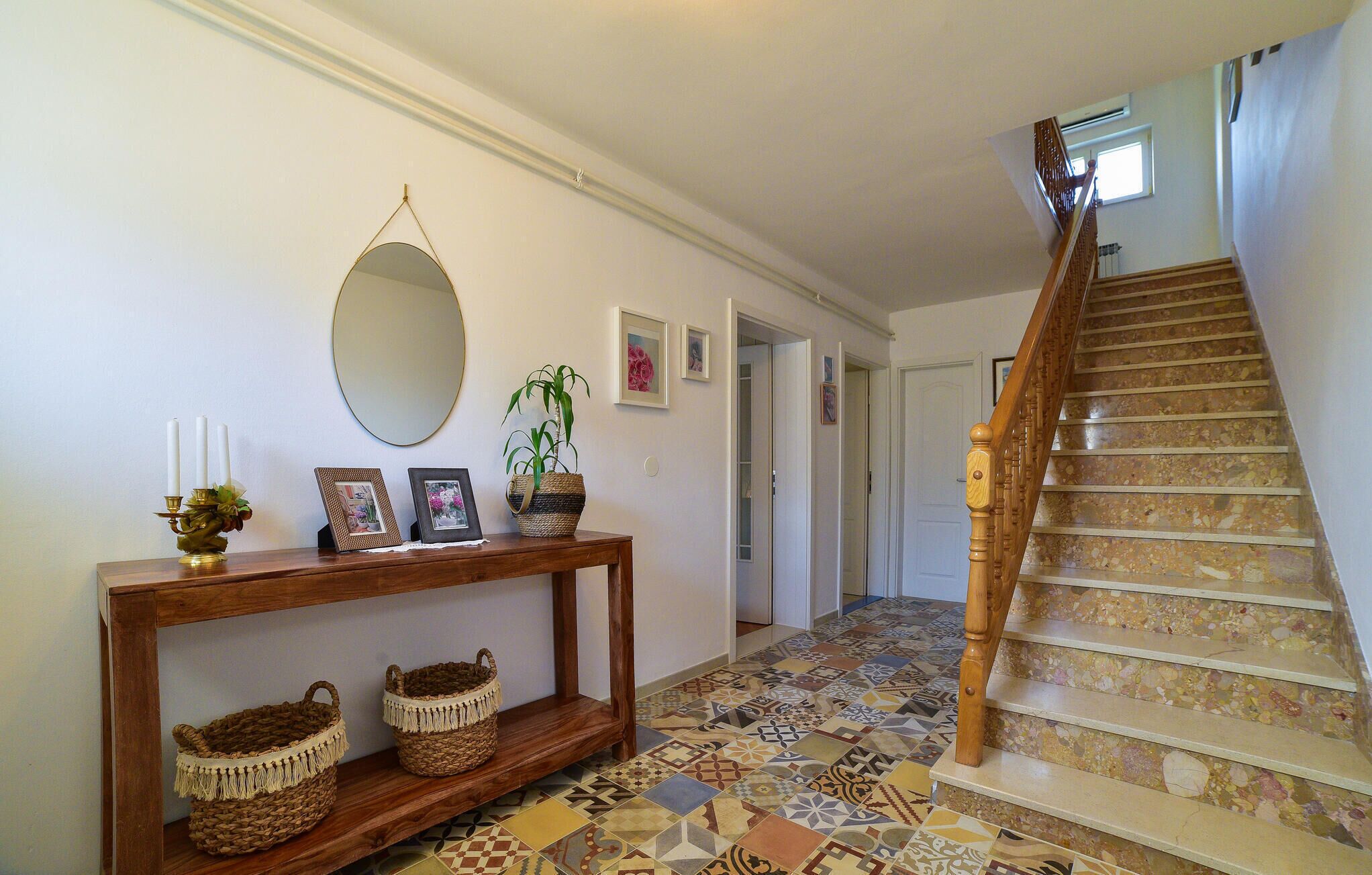 Un couloir avec une console en bois, des paniers en osier, un miroir et un escalier dont les marches sont recouvertes de mosaïques.