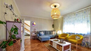 Una sala de estar con piso de madera, un sofá gris, un sillón amarillo, una mesa de centro blanca y una cesta de mimbre.