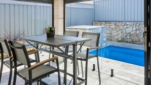 Een terras buiten met een tafel en stoelen, een zwembadje en een stenen muur.