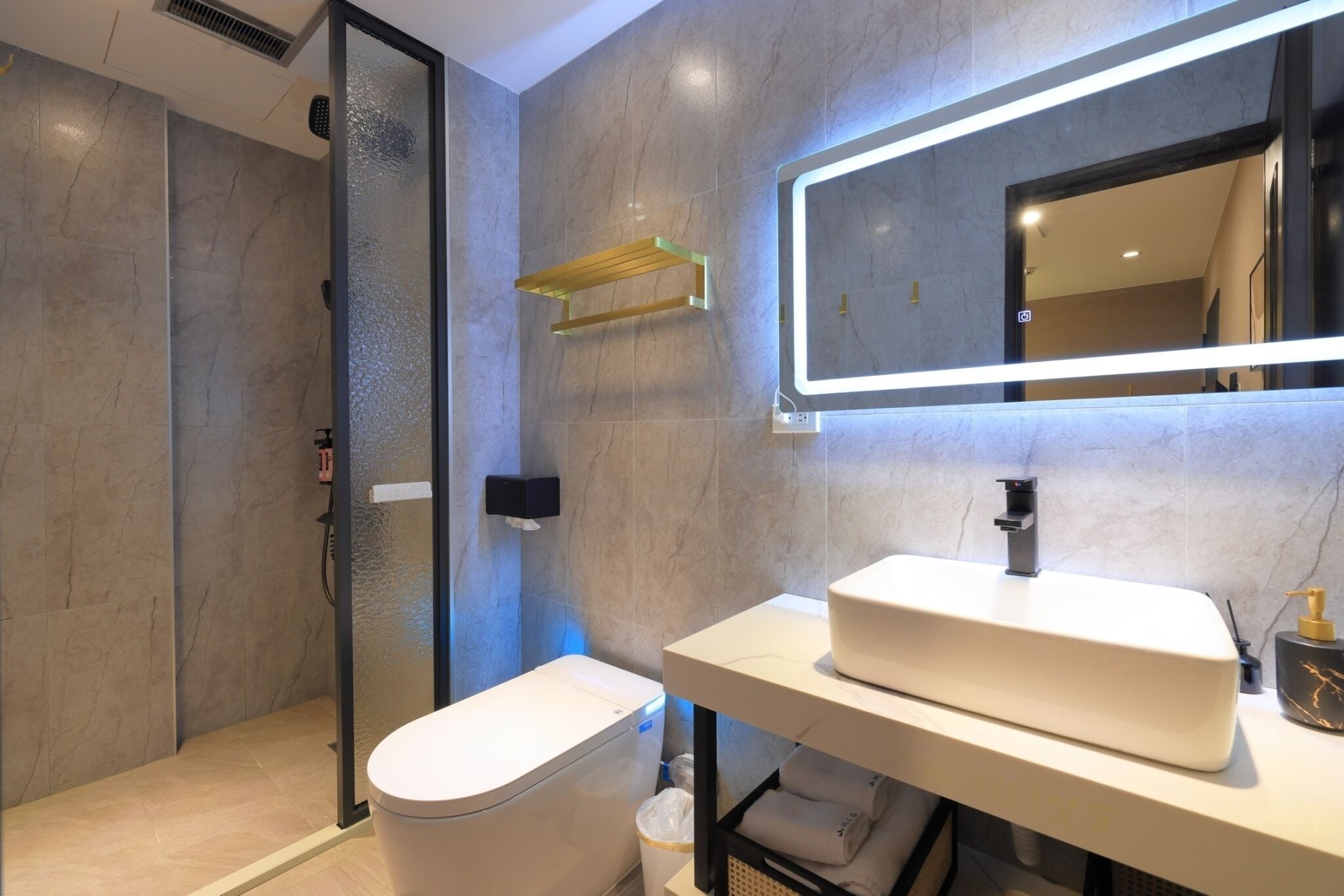 A modern bathroom with a glass-enclosed shower, a white sink, and a large mirror with integrated lighting.