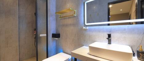 A modern bathroom with a glass-enclosed shower, a white sink, and a large mirror with integrated lighting.