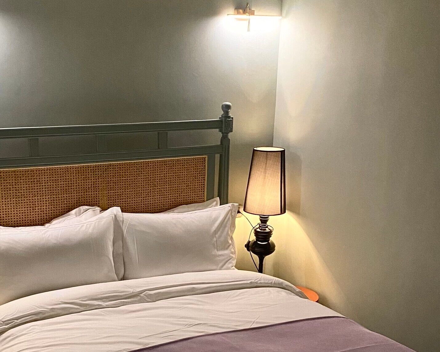 A bed with white linens, a wooden headboard, and a bedside lamp.