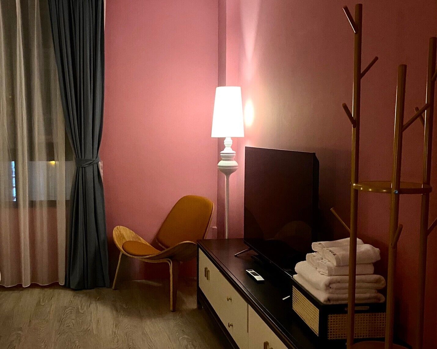 A hotel room with a bed, a TV, a chair, a lamp, and a shelf with towels.