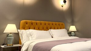 Quarto de hotel com cabeceira amarela com textura em botão, roupa de cama branca e duas luminárias fixadas na parede.
