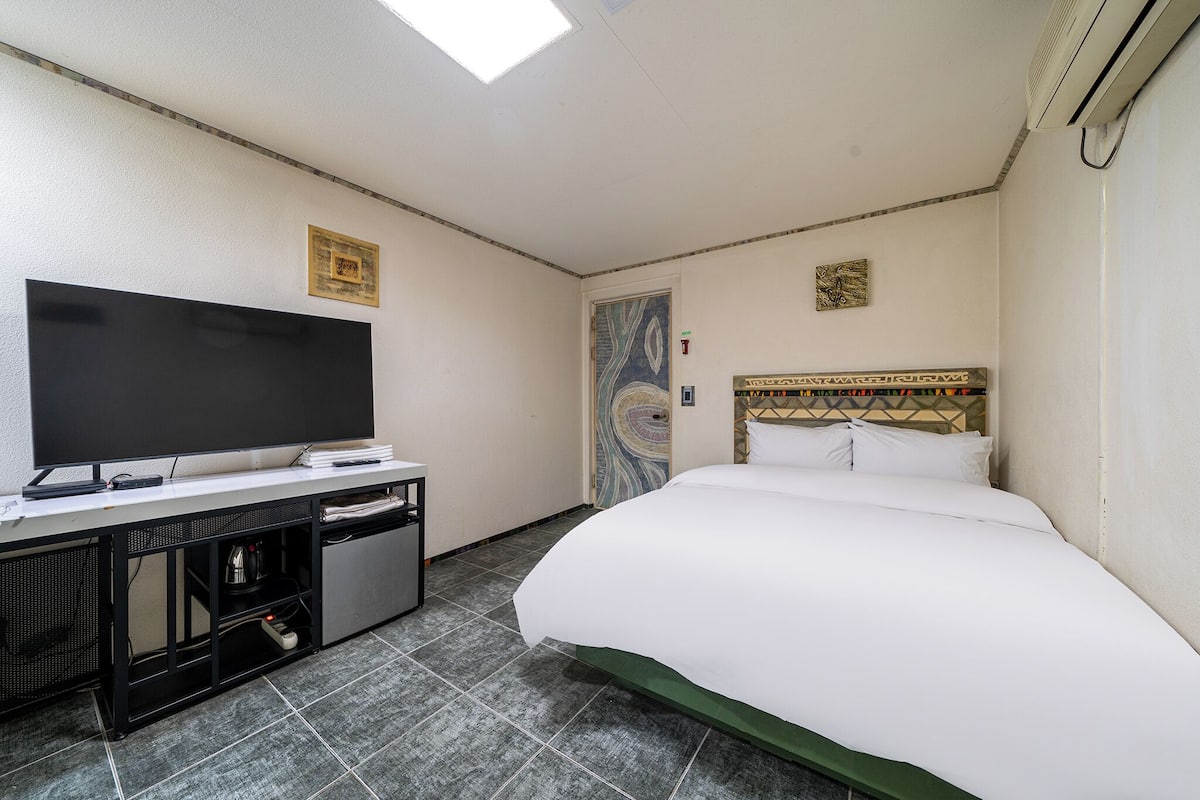 A hotel room with a bed, a TV, a desk, and a door.