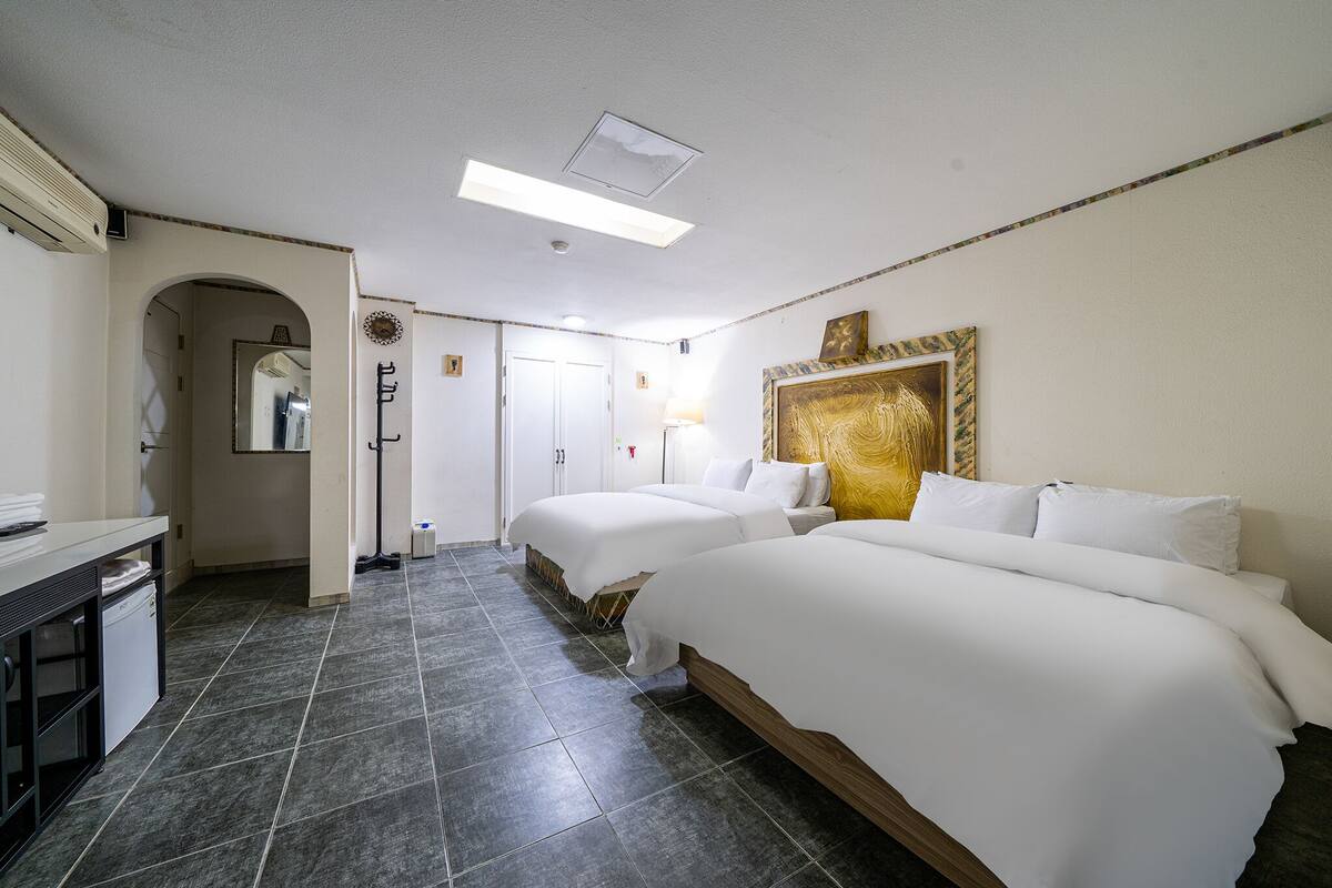 A hotel room with two beds, a desk, and a mirror.