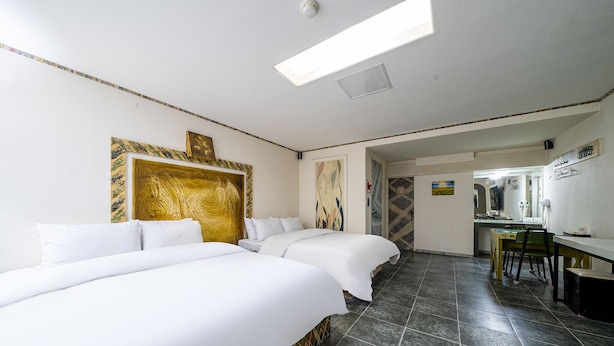 Ein Hotelzimmer mit zwei Betten, einem Schreibtisch und einem Stuhl. Ein großes Fenster und eine Tür zum Badezimmer.