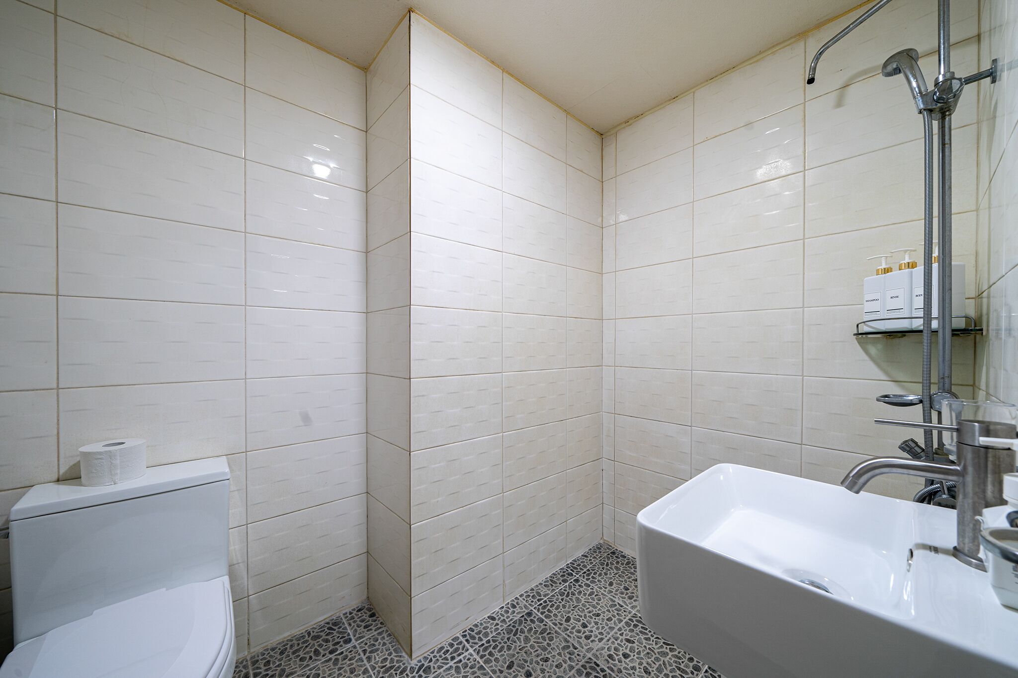 A bathroom with white tiled walls, a white sink, and a shower area.