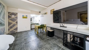 Ein kleines Hotelzimmer mit Bett, Schreibtisch mit Stuhl, Fernseher und einer Küchenzeile.