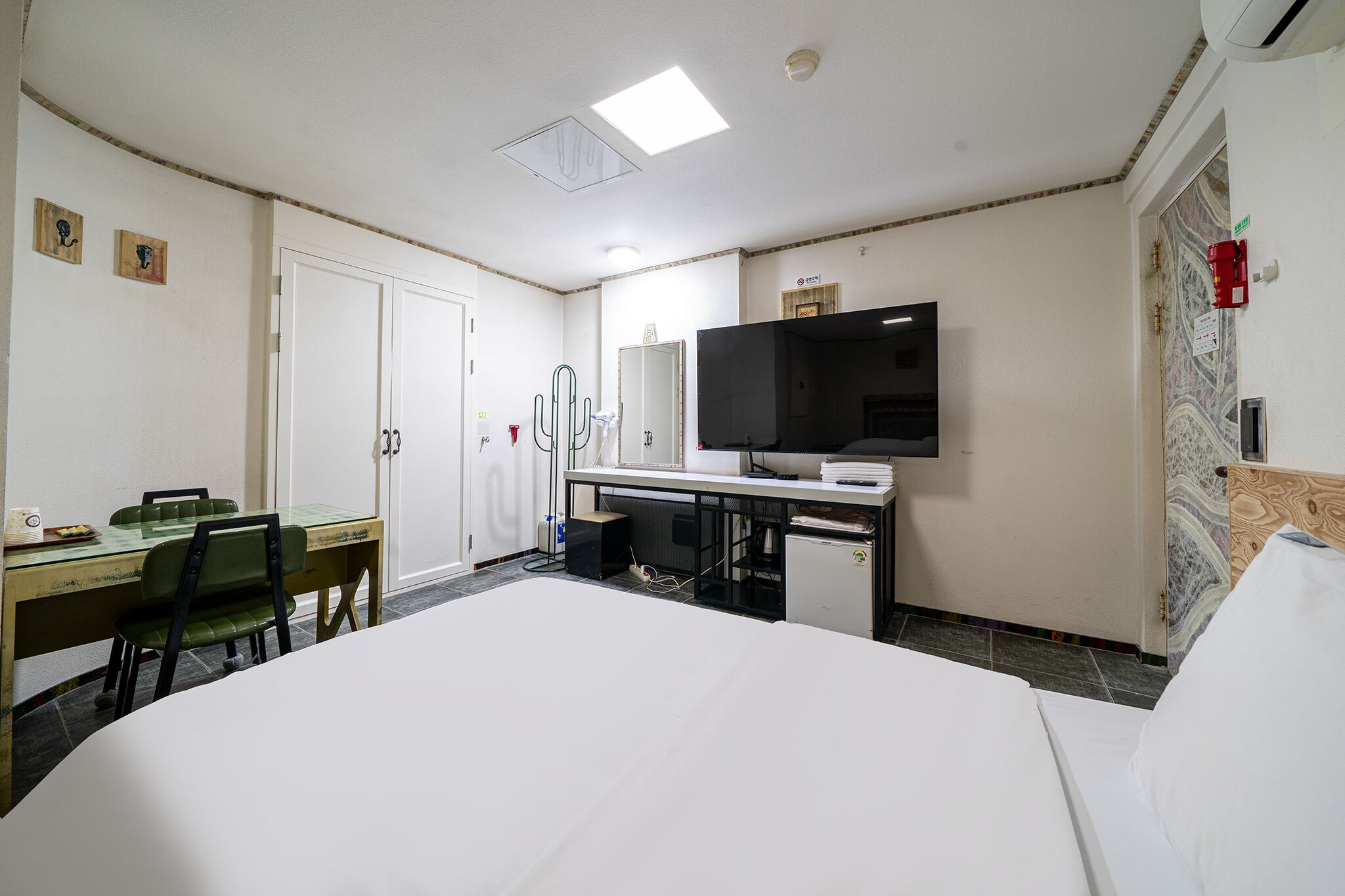 A hotel room with a bed, a desk with a computer, a television, and a small refrigerator.