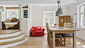 Ein geräumiges Zimmer mit einer Holztreppe, einem Esstisch mit Stühlen, einem roten Sofa und einem Holzschrank.