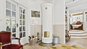 Ein geräumiges Wohnzimmer mit einem großen Kamin, einem roten Samtstuhl, Holzdielen und Blick ins Freie.