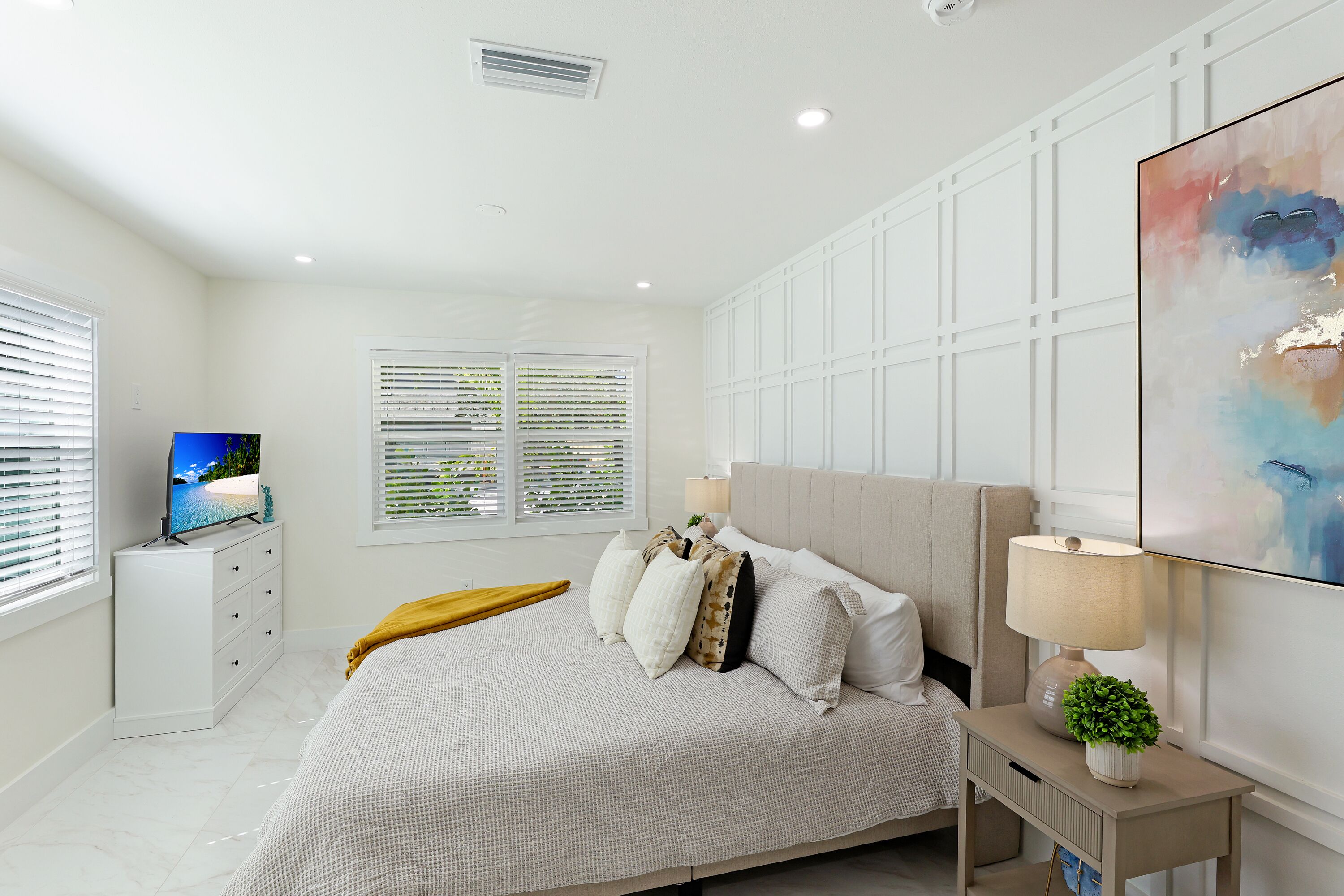 A bedroom with a bed, bedside table, lamp, and a TV on a dresser.