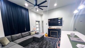A modern living room with a sectional sofa, a fireplace, a flat-screen TV, and a ceiling fan.