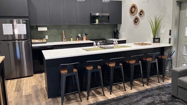 A modern kitchen with dark cabinets, a large island with bar stools, and pendant lighting.