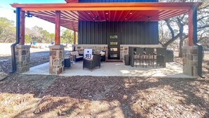 A covered outdoor seating area with stone pillars, a stone wall, and a door with a logo.
