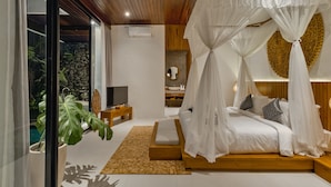 A modern bedroom with a canopy bed, a stone wall, a sink, and a television. - Abhinaya Ubud Villa (Ubud)