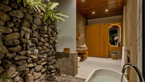 A modern bathroom with a stone wall, a bathtub, wooden accents, and a wooden ceiling. - Abhinaya Ubud Villa (Ubud)