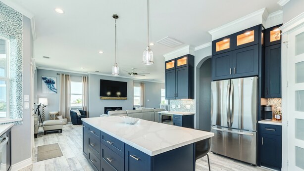 Una cocina moderna con armarios azul oscuro, una isla grande, electrodomésticos de acero inoxidable e iluminación colgante.