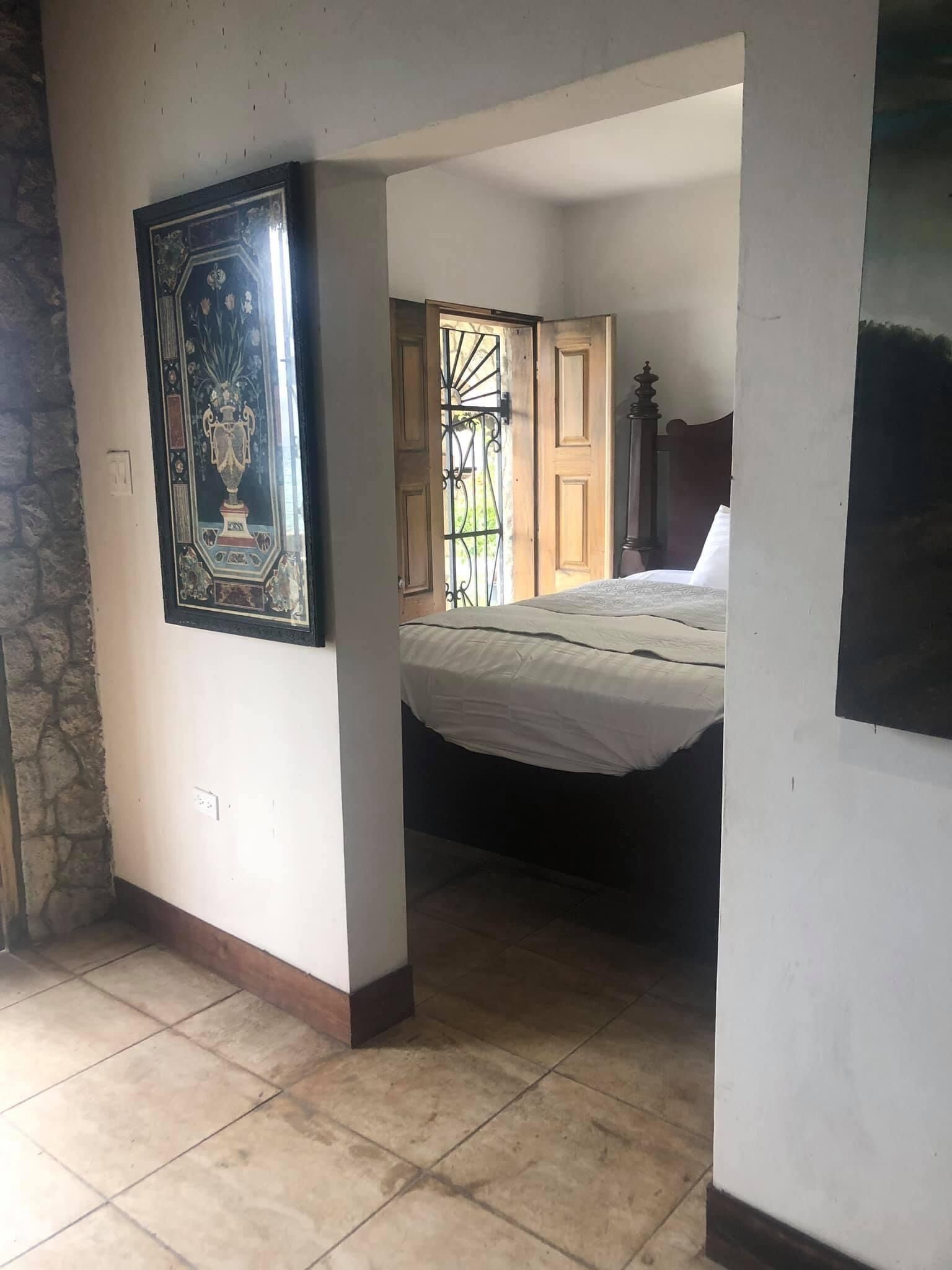 A bedroom with a bed, a door leading to another room, and a tiled floor.