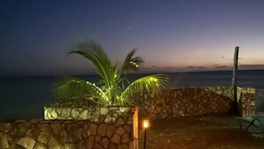 A stone wall with a palm tree and a lit lamp post at dusk. - The Belair SeaSide Villas. 4 suites, 2 guests per Suite. 1, 2/bedroom/3 guests (Belmont)