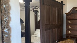 A bedroom with a large wooden door, a four-poster bed, and a classic chair. - The Belair SeaSide Villas. 4 suites, 2 guests per Suite. 1, 2/bedroom/3 guests (Belmont)