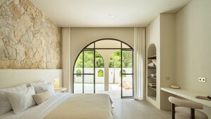 A modern hotel room with a large bed, a desk, and a view of a pool and greenery through a glass door.