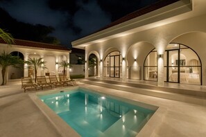 A poolside area with a swimming pool, lounge chairs, and a covered patio with arched doorways.