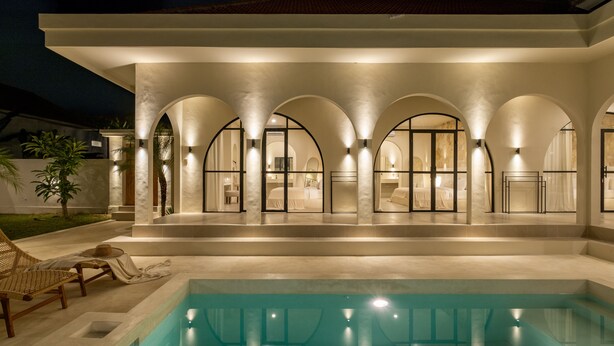 A modern building with a swimming pool, arched windows, and outdoor seating.
