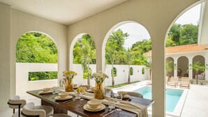 A dining area with a pool view, featuring a wooden table set with plates, glasses, and flowers.
