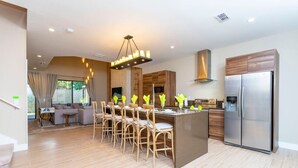 A modern kitchen with a central island, stainless steel appliances, and a dining area with wooden chairs. - Luxury 3BDR House near Disney! (Kissimmee)