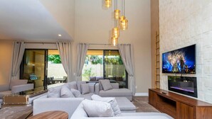 A modern living room with a sectional sofa, a TV mounted on a white brick wall, and a glass door leading to an outdoor area. - Luxury 3BDR House near Disney! (Kissimmee)