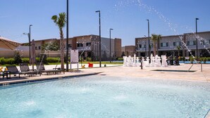 A pool area with water jets, lounge chairs, and a building in the background. - Luxury 3BDR House near Disney! (Kissimmee)