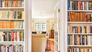 Une pièce avec un canapé beige, un plancher en bois et des étagères remplies de livres.