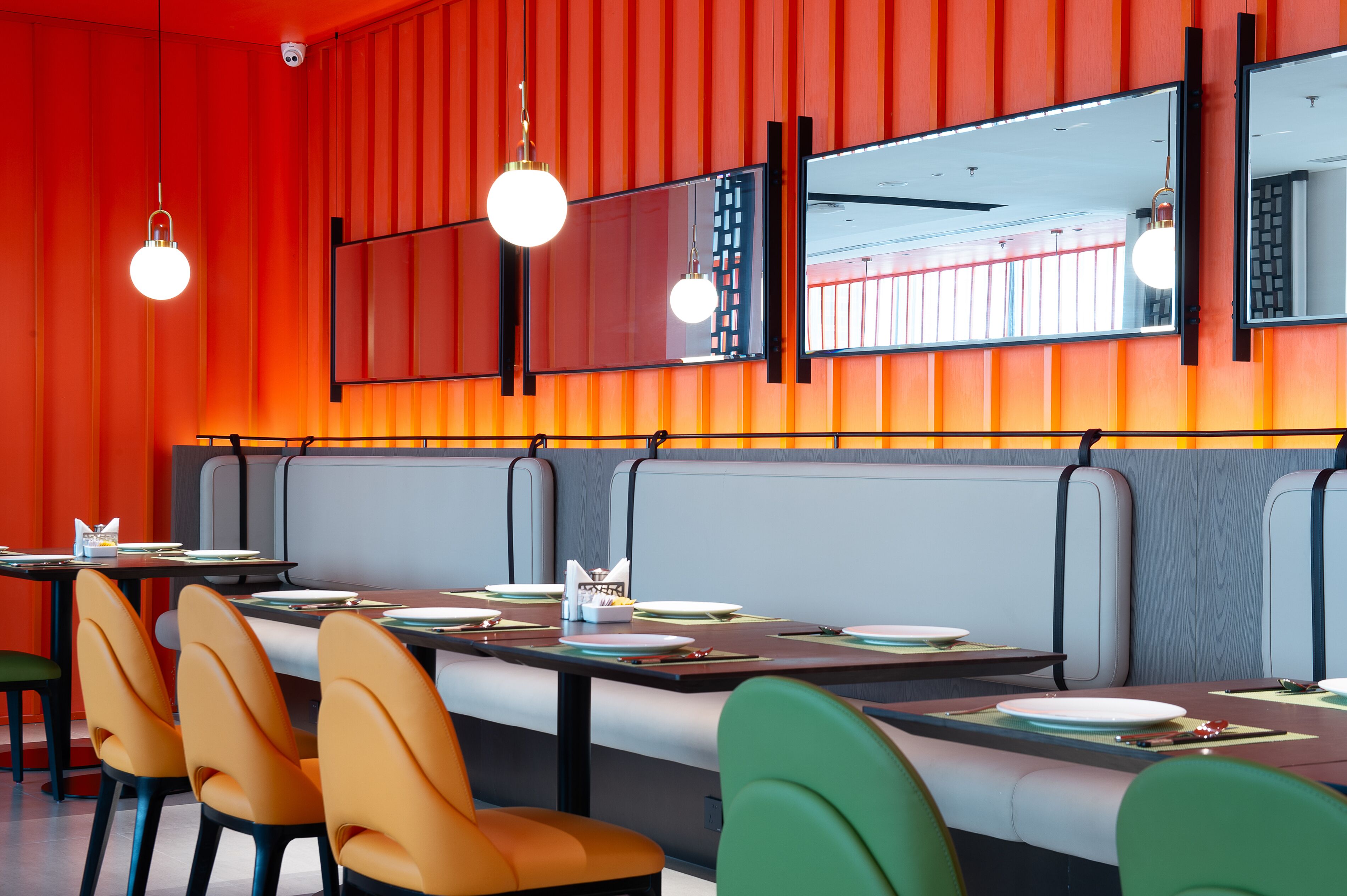 A restaurant with booths, orange and green chairs, and a red wall with vertical stripes.