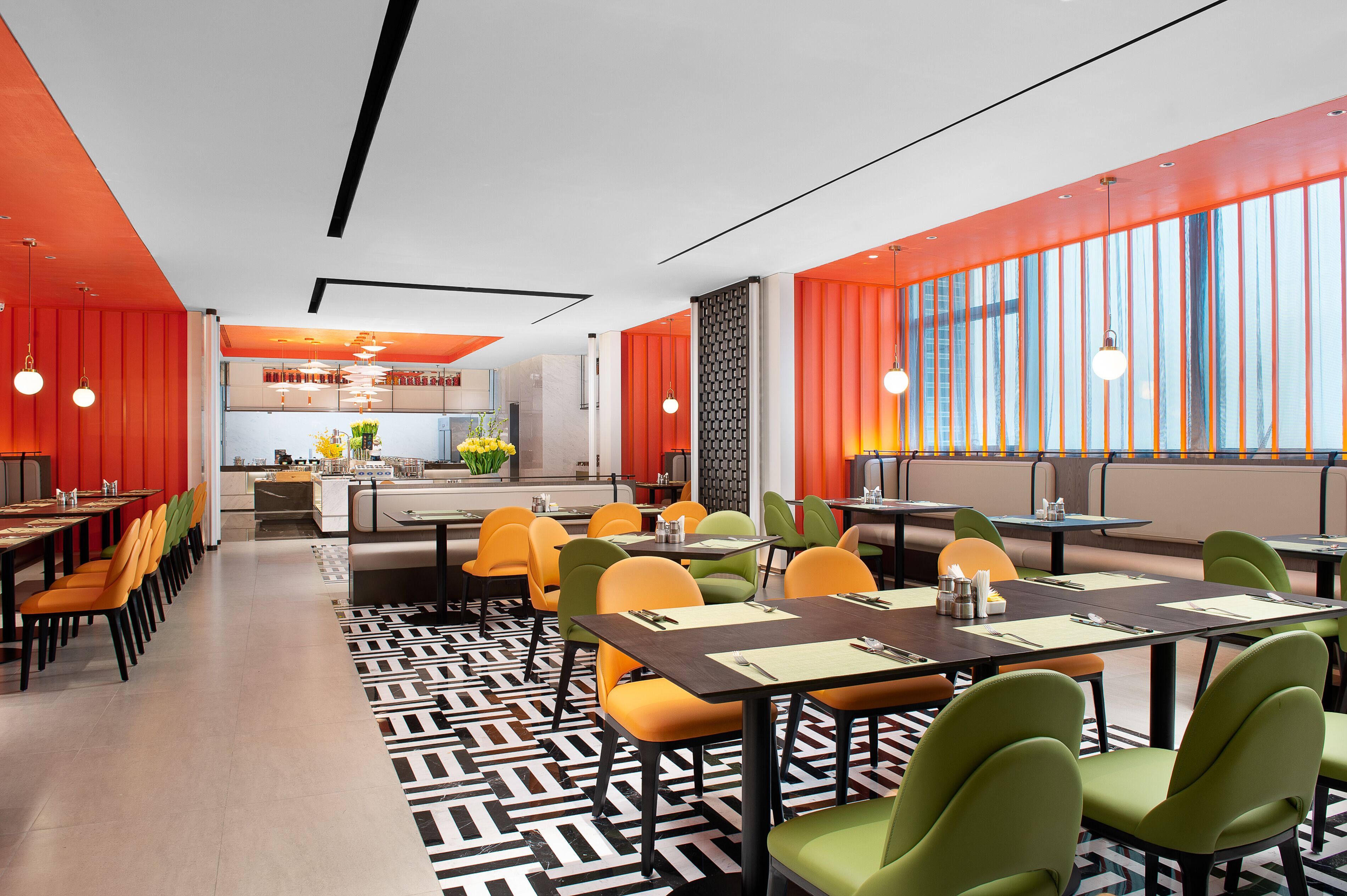 Un restaurante moderno con suelo de diseño geométrico, sillas naranja y verde, y una zona central de comedor con mesas.