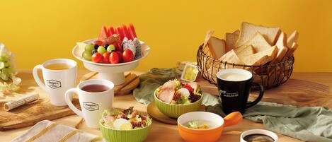 A breakfast setting with various food items and drinks on a wooden table against a yellow background.
