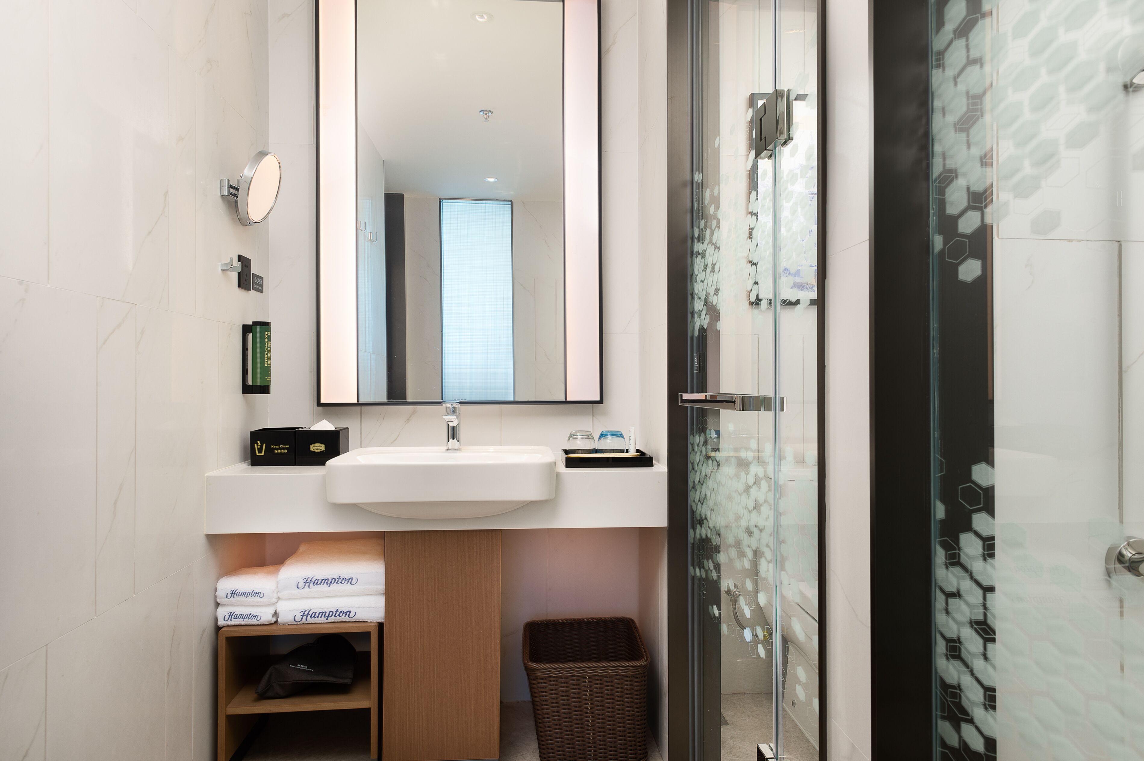 Un baño moderno con un lavamanos blanco, espejo y cabina de ducha de vidrio.