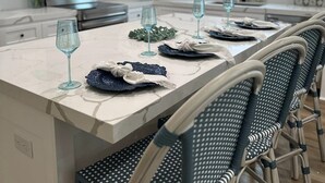 Une cuisine moderne avec des meubles blancs, un îlot en marbre et des chaises en osier.