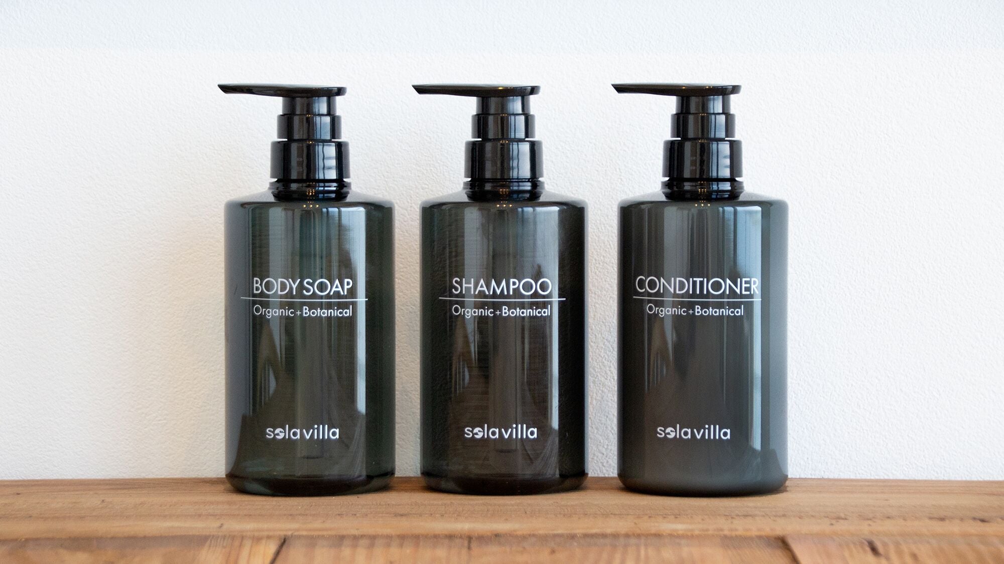 Three black bottles of Solavilla body products on a wooden surface.