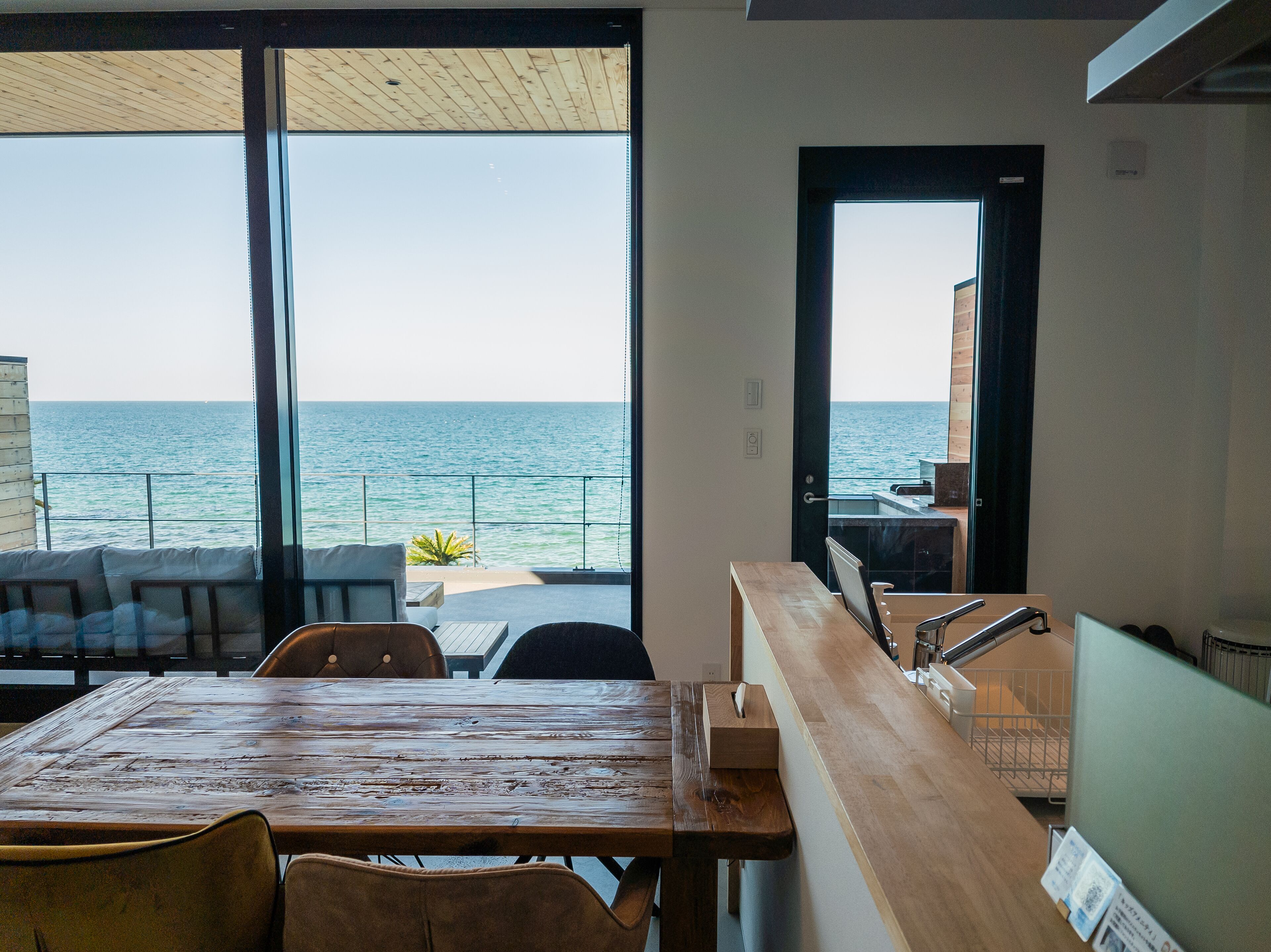 A dining area with a view of the sea, a wooden table, and chairs.