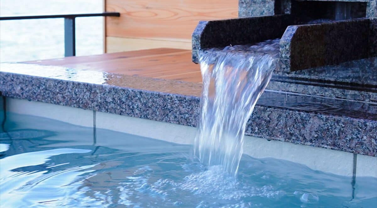Una fuente de agua con un flujo en cascada hacia una piscina, rodeada por una estructura de piedra.