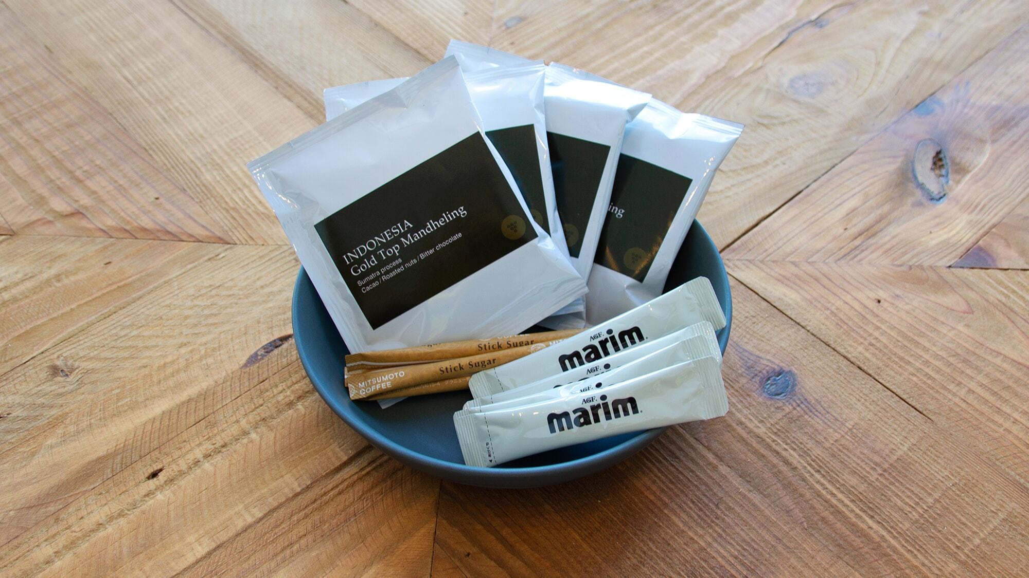 A bowl containing several packets of 'Indonesia Gold Top Mandheling' coffee and 'Mitsumoto Coffee' sticks.