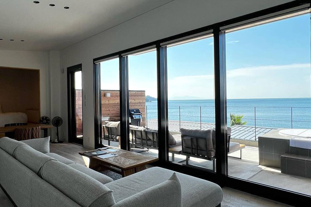Een moderne woonkamer met een grote schuifpui naar een balkon met uitzicht op zee.