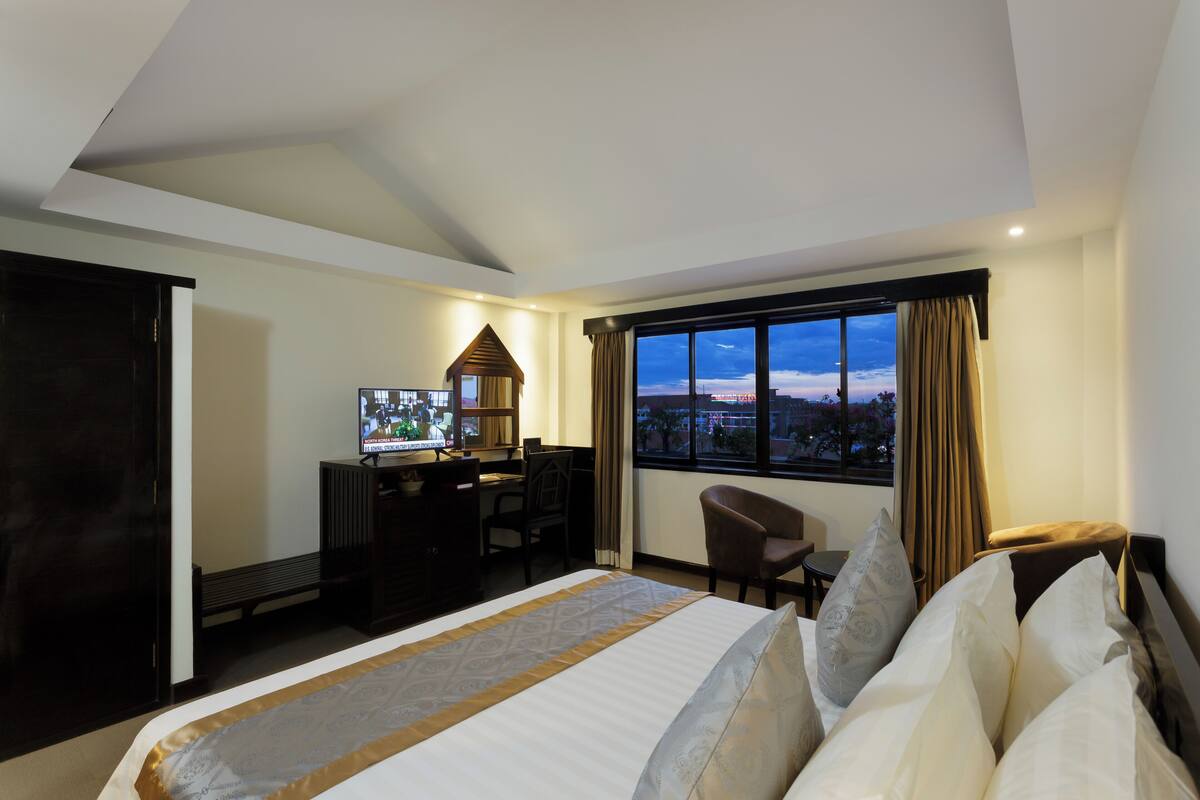 Una habitación de hotel con cama, escritorio, silla, televisor y un ventanal con vistas a la ciudad.