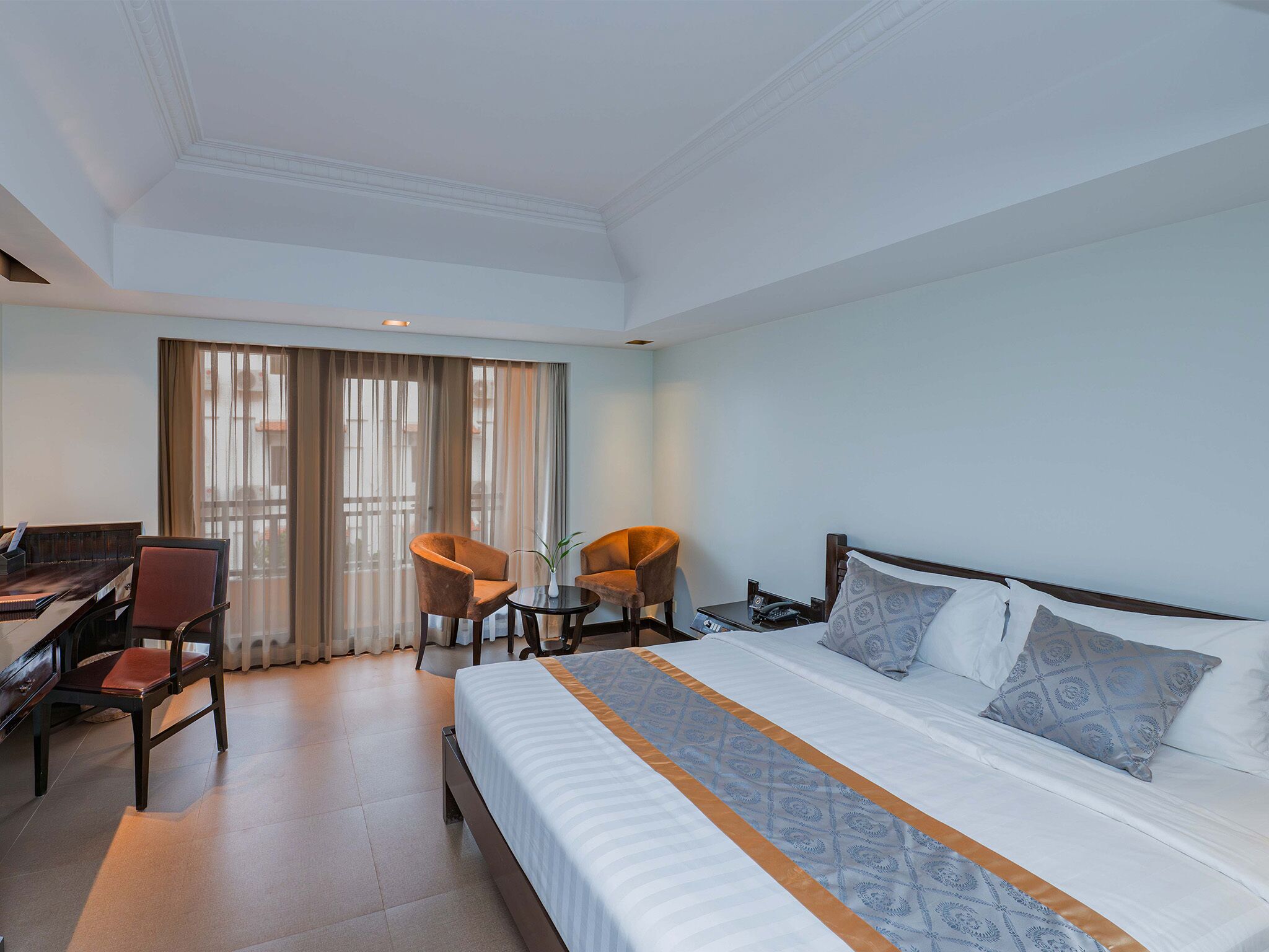 A hotel room with a bed, desk, chairs, and a large window.