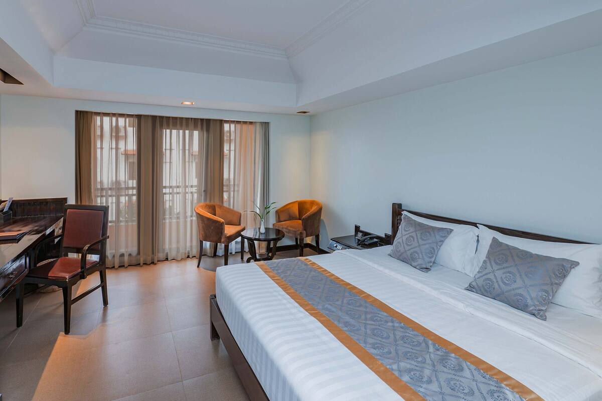 Habitación de hotel con cama, escritorio, sillas y un ventanal grande.