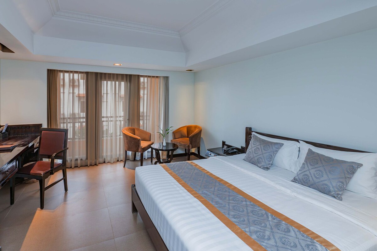 Habitació d'hotel amb llit, escriptori, cadires i una finestra gran.