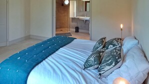 Un dormitorio con cama, almohadas, una lámpara de noche y un baño visible a través de una puerta abierta.
