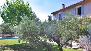 Una casa con techo de tejas, piscina y jardín con olivos.